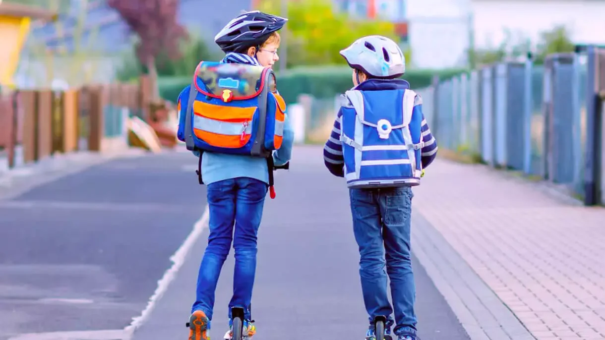 Two children on scooters, wearing helmets, whilst talking to each other