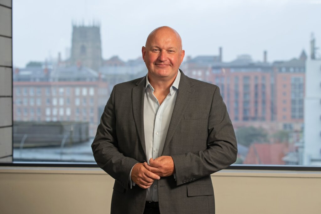 A headshot image of Graham Sant, stood in front of a window that has Nottingham Skyline in the background