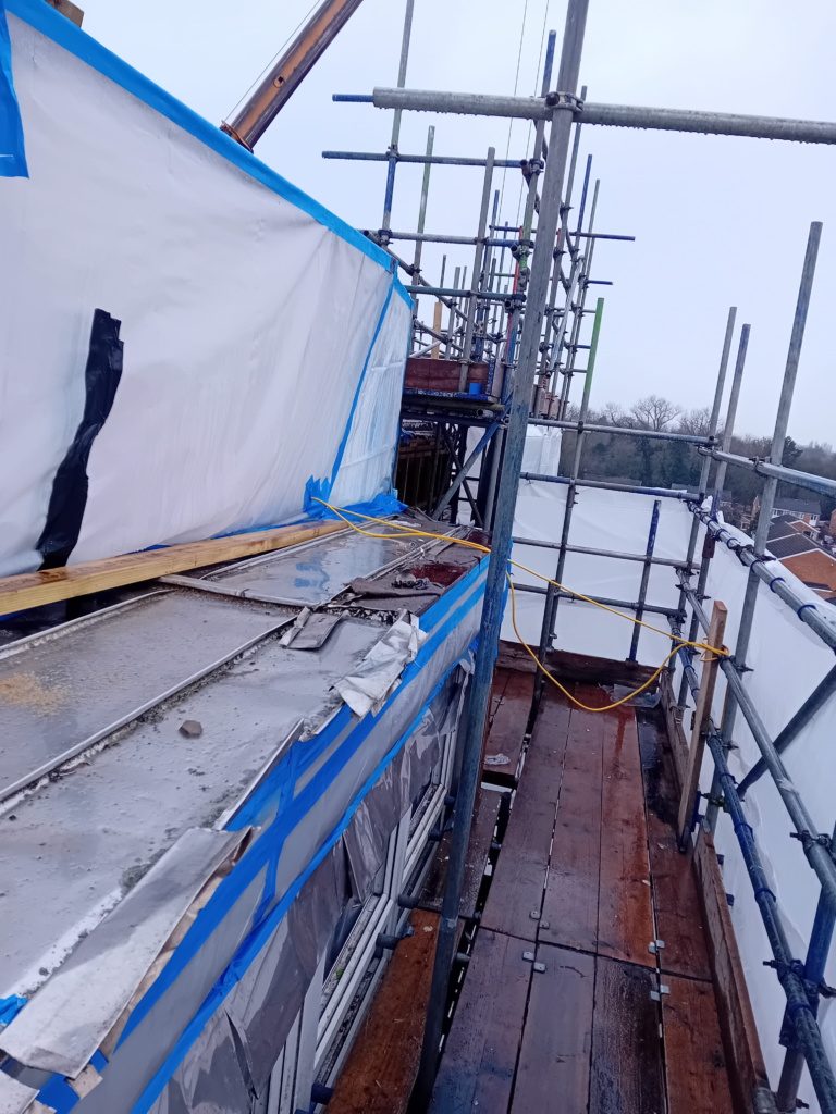 Plastic sheeting on the left hand side with the centre and right hand side of the image taken up by scaffolding and wooden walk planks